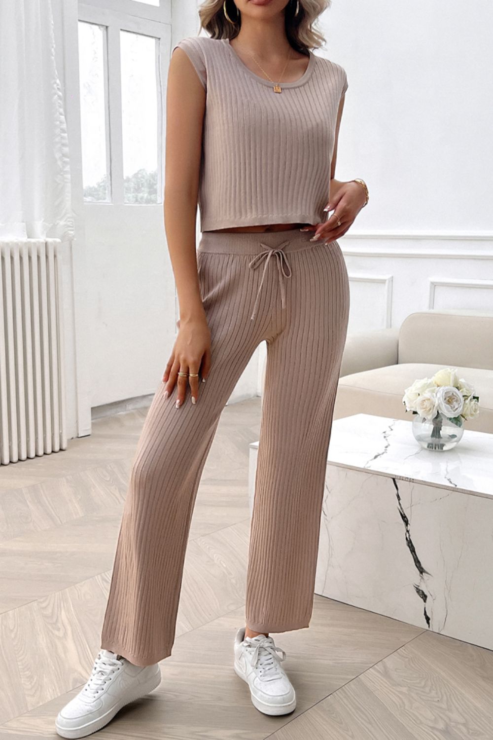 Woman wearing beige ribbed round neck top and matching pants set with tie waist and white sneakers indoors